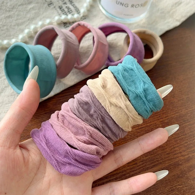 A hand holds a stack of extra-wide elastic hair bands in various shades of purple and teal.