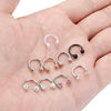 A hand displays a set of crystal horseshoe barbell rings made of surgical steel.