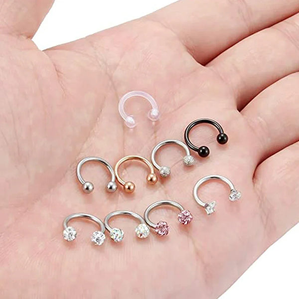 A hand displays a set of crystal horseshoe barbell rings made of surgical steel.