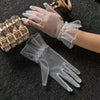 A hand wearing sheer white lace tulle finger gloves is shown next to a gold-toned accessory.