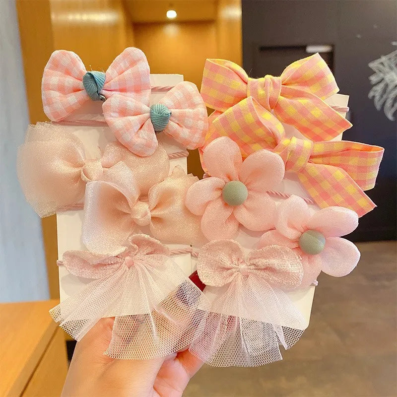 A hand holds a display of pink and yellow flower bow hair ties for girls.