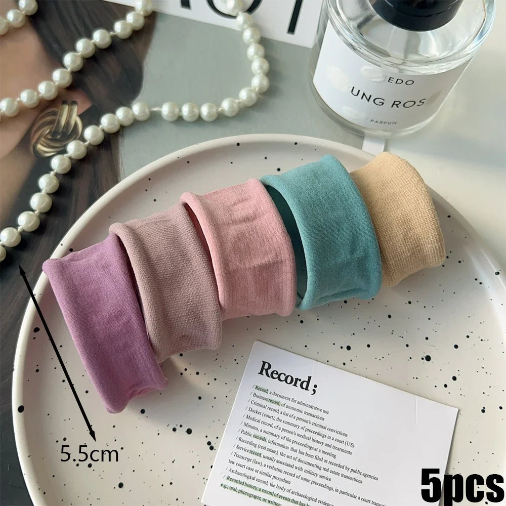 A collection of five pastel colored elastic hair bands arranged on a white plate.