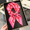 A pink and red patterned silk scarf tied in a bow displayed in a black square frame.