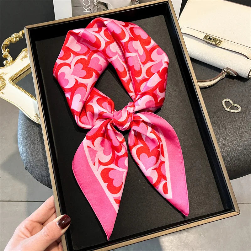 A pink and red patterned silk scarf tied in a bow displayed in a black square frame.