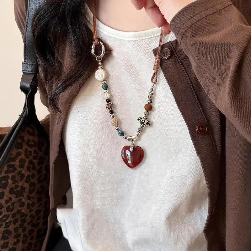 A close-up of a bohemian heart beaded pendant necklace worn by a person, featuring various beads and a reddish-brown heart ch