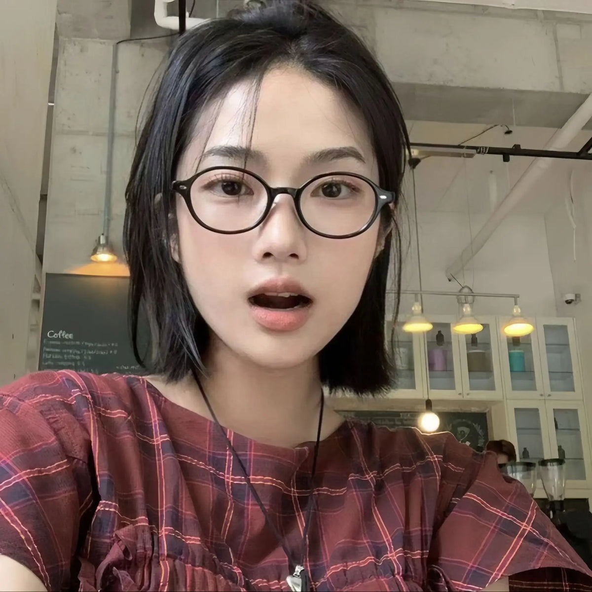 A close-up portrait of a woman wearing round anti-blue light computer glasses and a plaid shirt.
