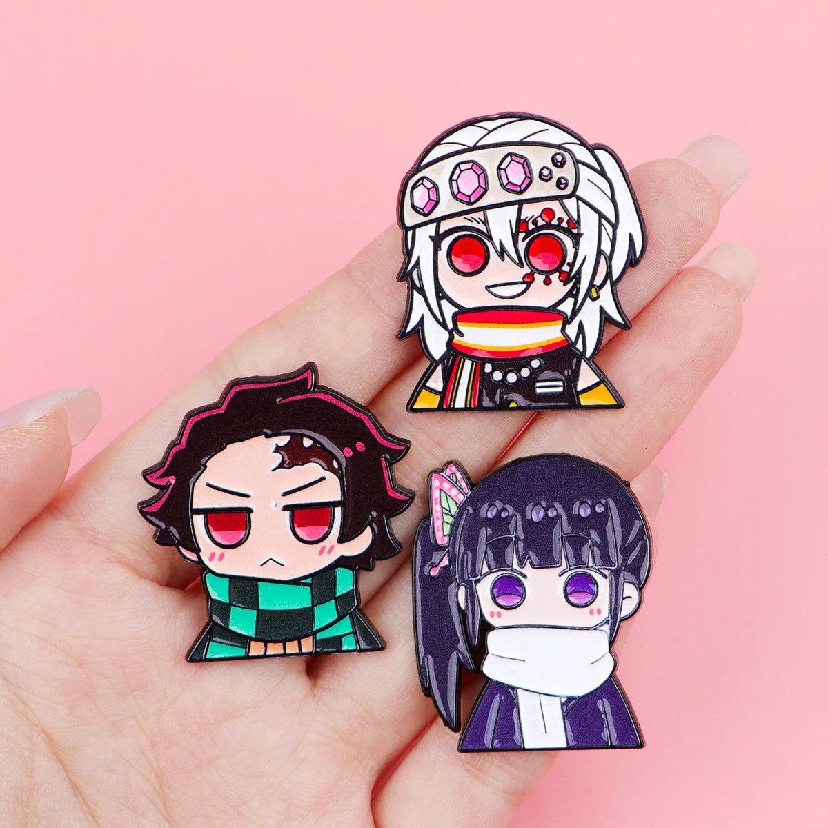 A hand holds a set of 12 anime enamel pin brooches featuring characters with distinct hairstyles and facial expressions.