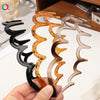 A hand holds several fashion acetate toothed headbands in shades of amber, brown, and clear.