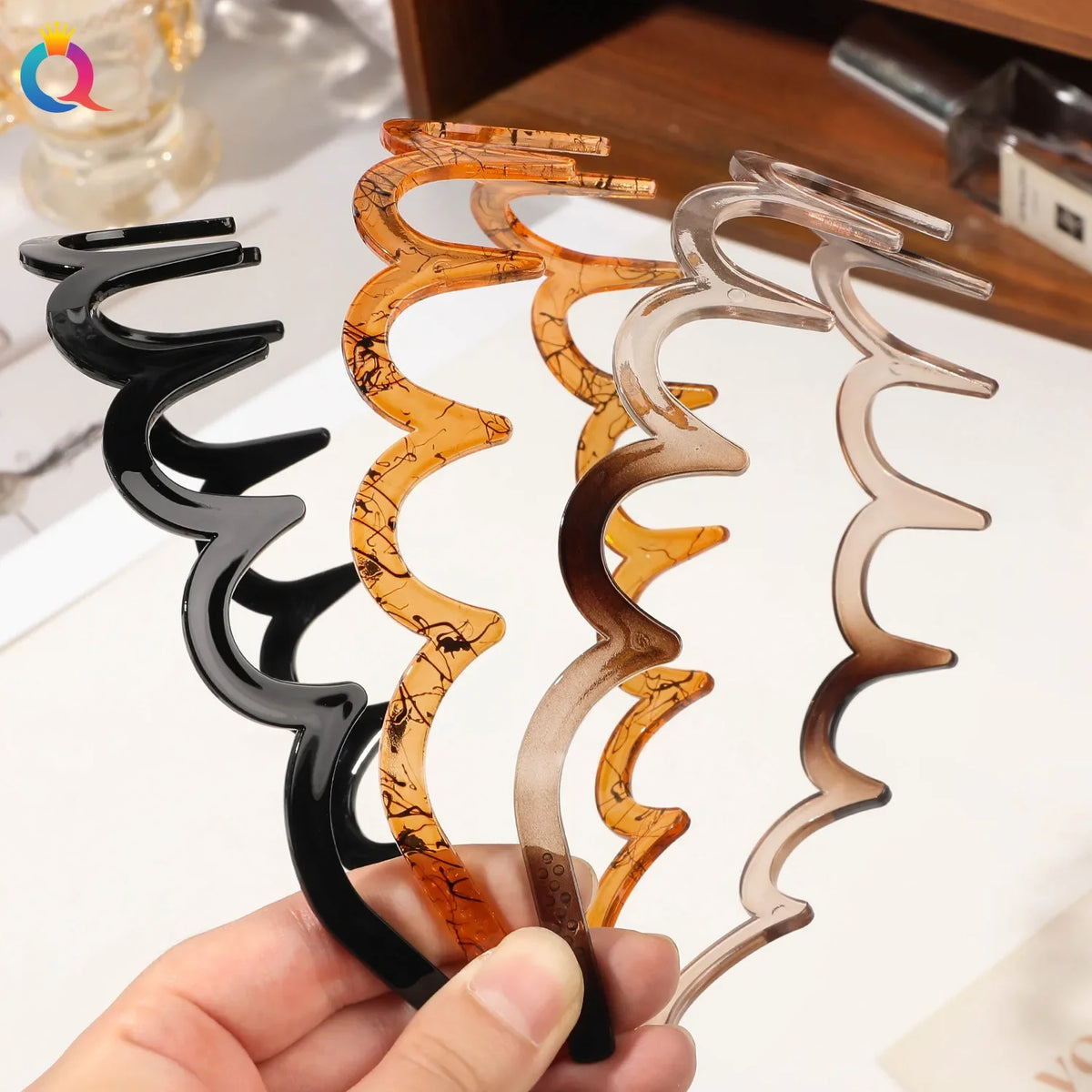 A hand holds several fashion acetate toothed headbands in shades of amber, brown, and clear.