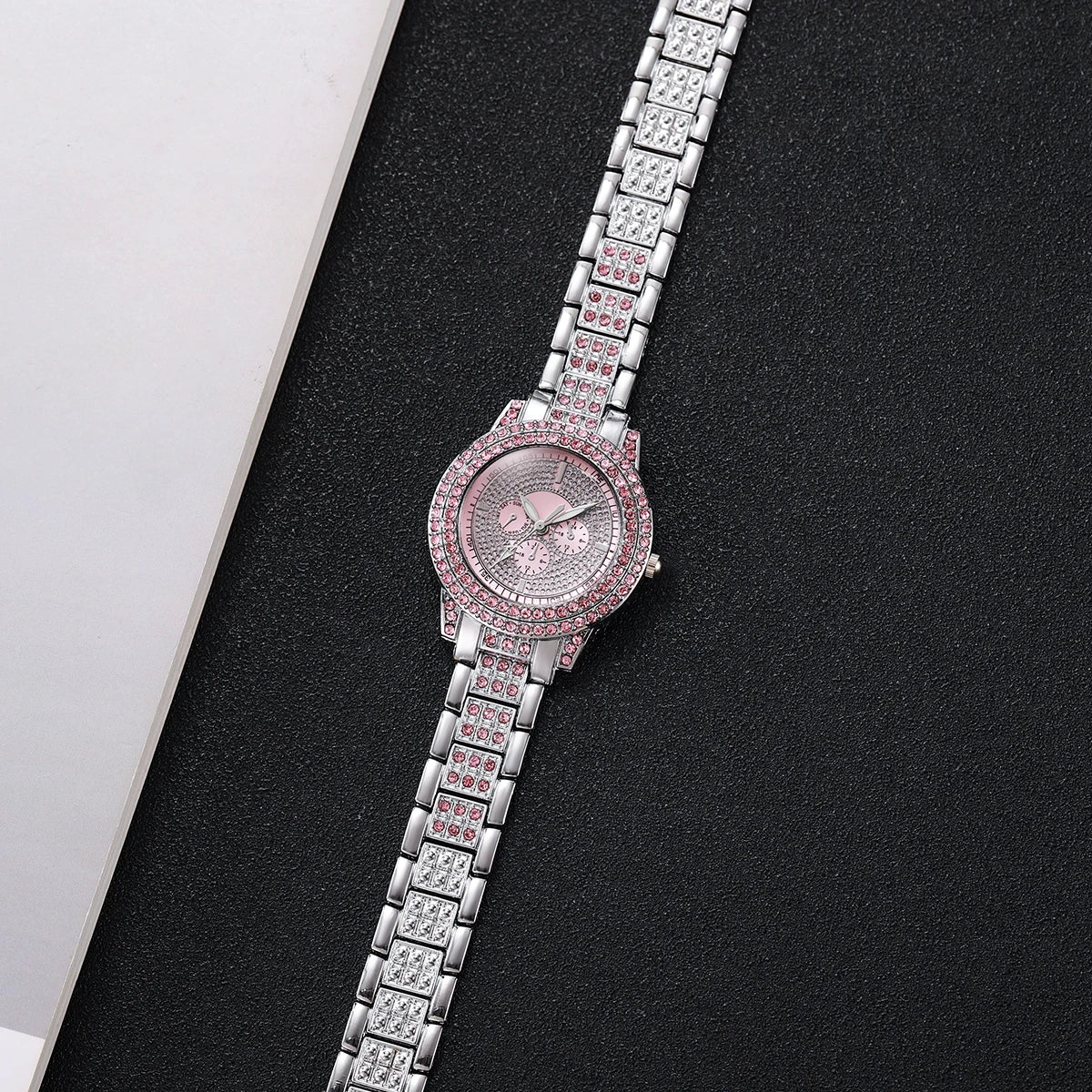 A silver-toned watch with a pink diamond rhinestone bezel and a matching bracelet on a black background.