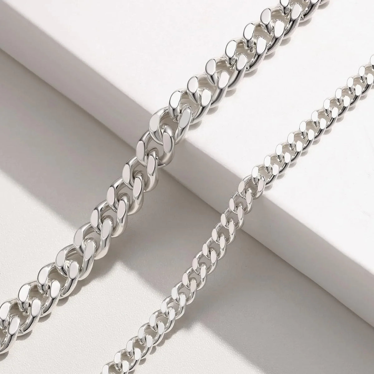 Silver gold plated minimalist Cuban link anklets laid diagonally on a white surface.