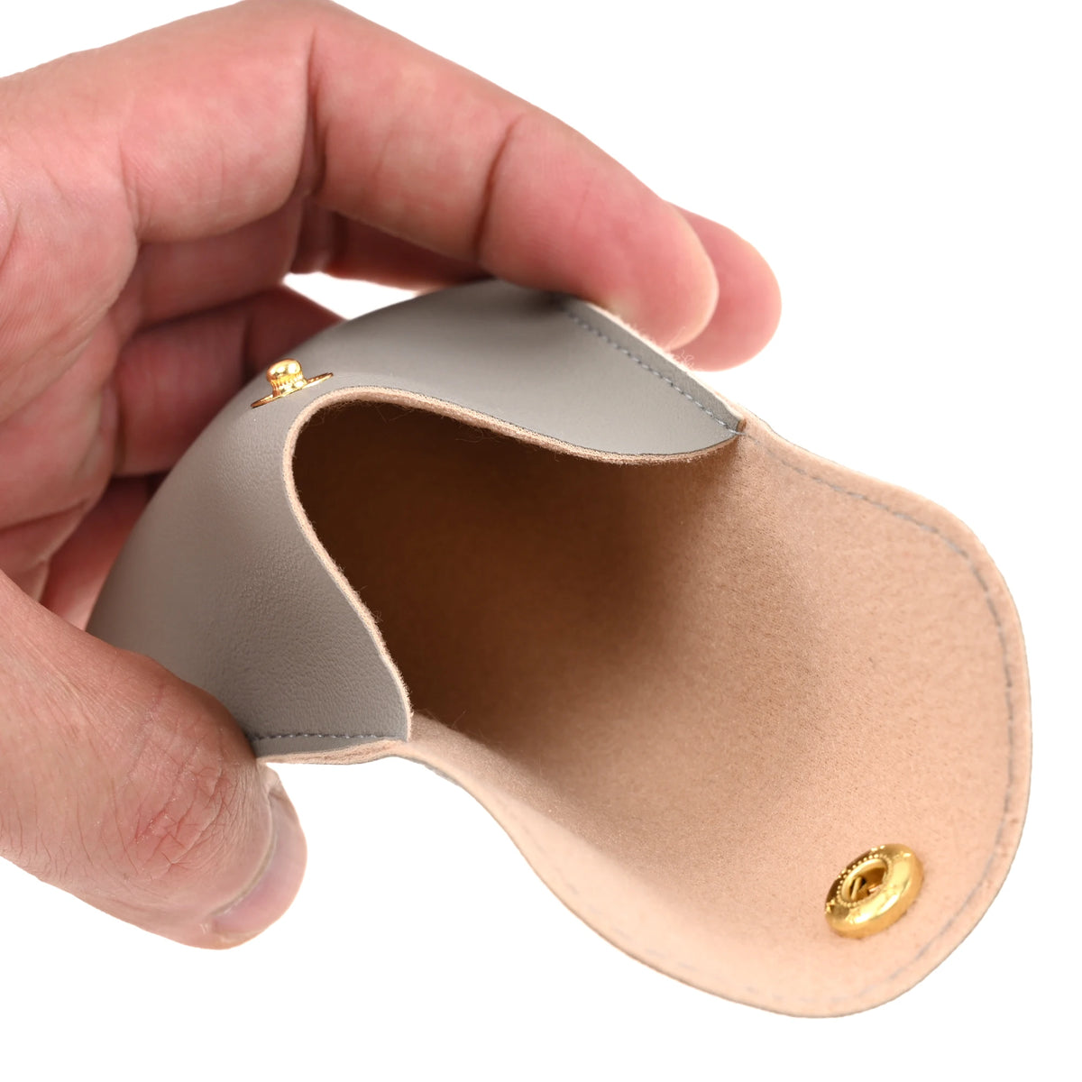 A hand holds a light beige PU leather jewelry pouch with a secure gold snap button.