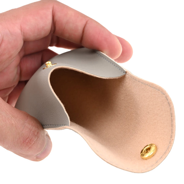 A hand holds a light beige PU leather jewelry pouch with a secure gold snap button.