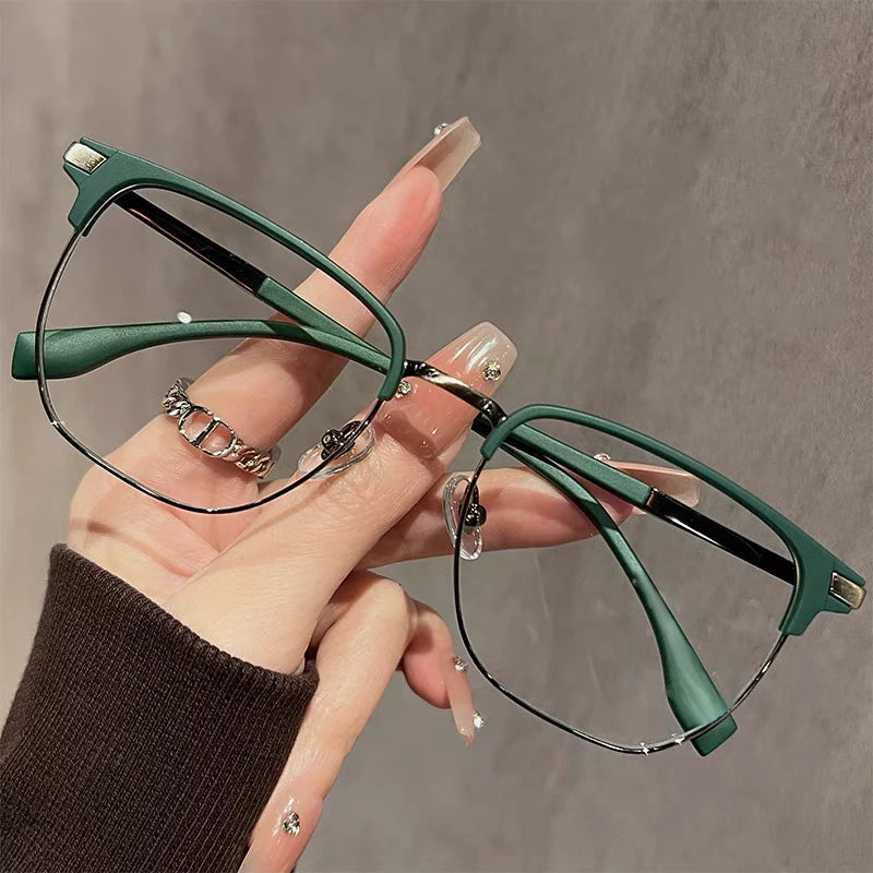 Eine Hand hält eine dunkelgrüne Anti-Blau-Licht-Lesebrille vor einem neutralen grauen Hintergrund.
