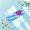 Collection de étoiles de mer et coquillages dorés dispersés sur fond bleu clair avec un élastique à cheveux rayé violet.
