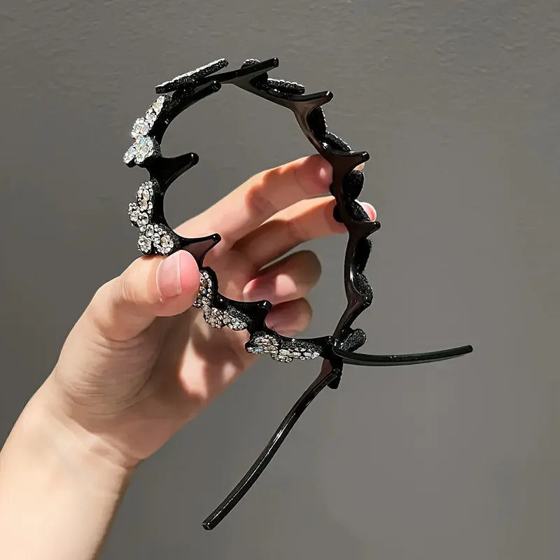 A hand holds a black, claw-like hair accessory decorated with clear rhinestones shaped like butterfly wings.