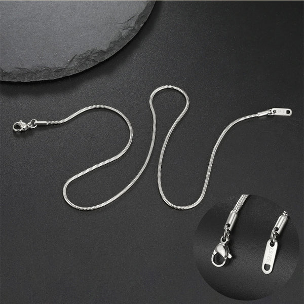 A silver stainless steel snake chain necklace is displayed against a dark background with a close-up of the pendant.