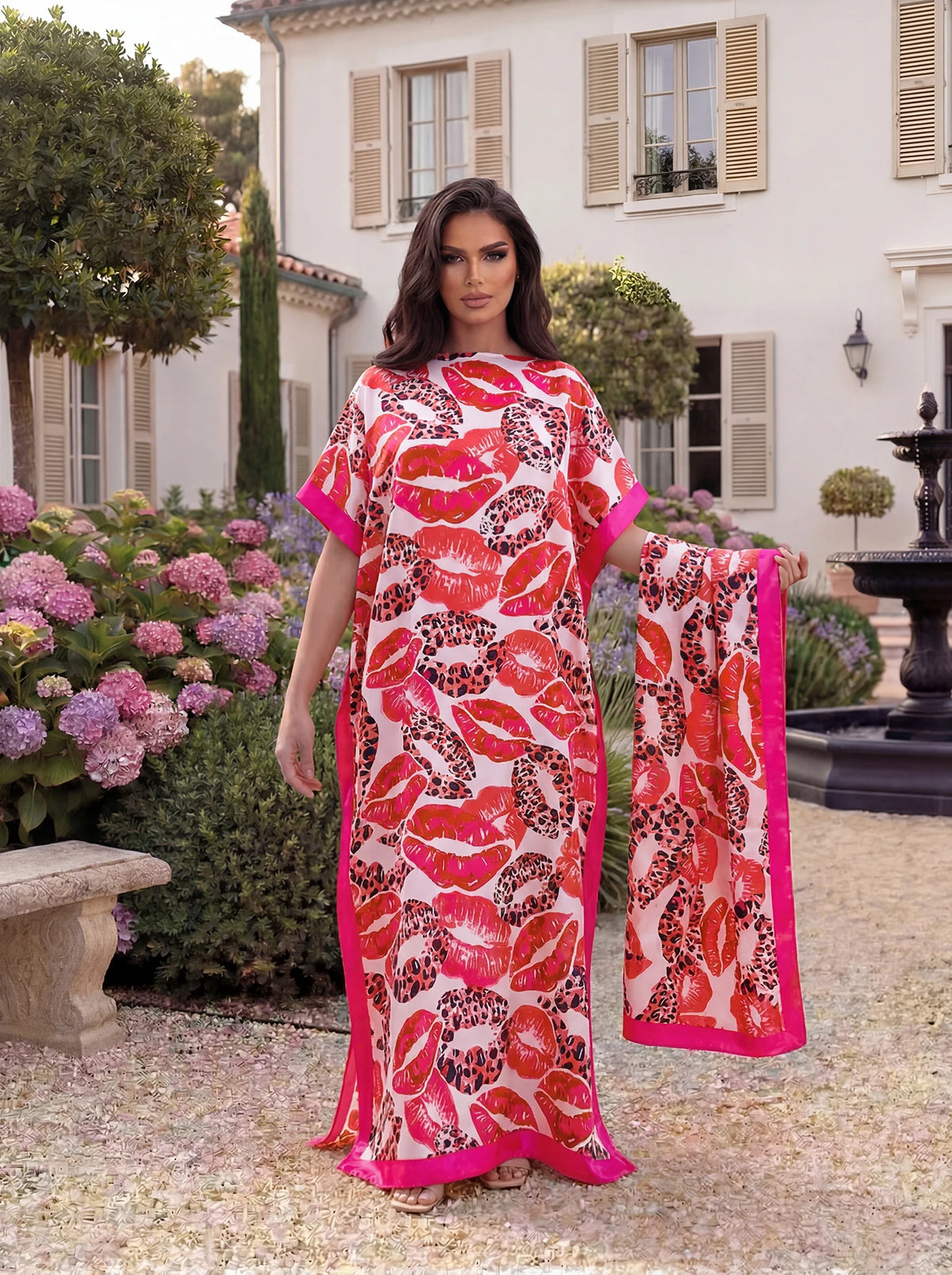 Eine Frau modelliert ein leuchtend orangees und pinkes Leopardenmuster-Satinstoff-Abaya-Schal-Set im Garten.