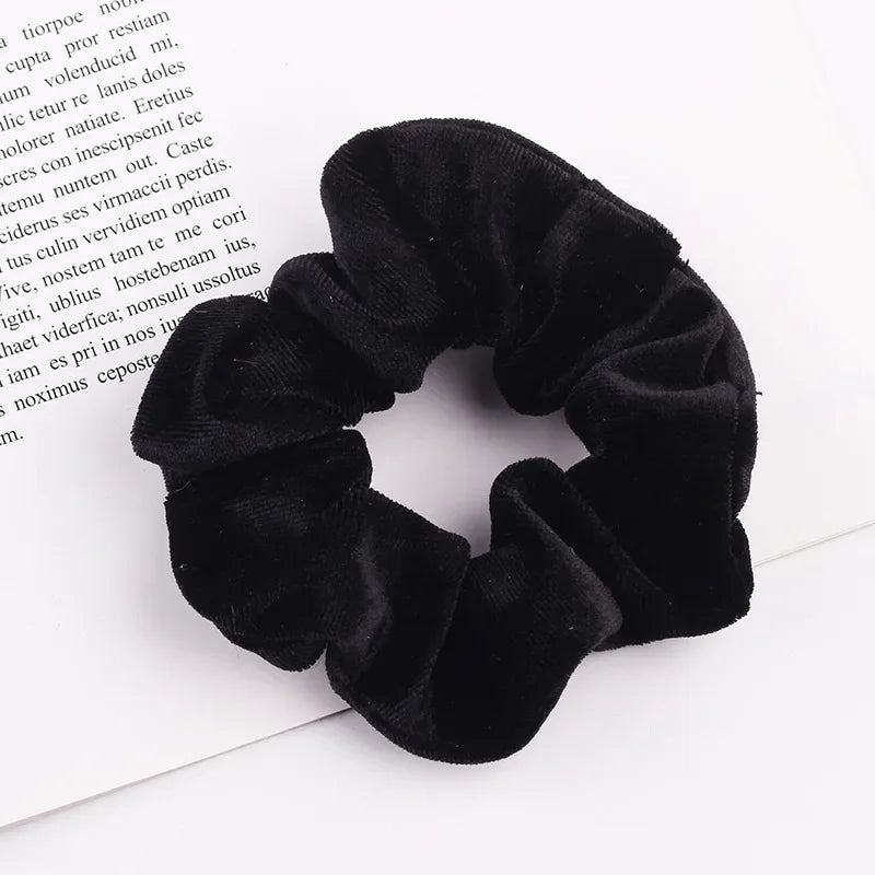 A close-up shot of a black velvet scrunchie, a soft elastic hair tie for women.