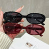 A hand holds a pair of brown tinted cat eye sunglasses against a light background.