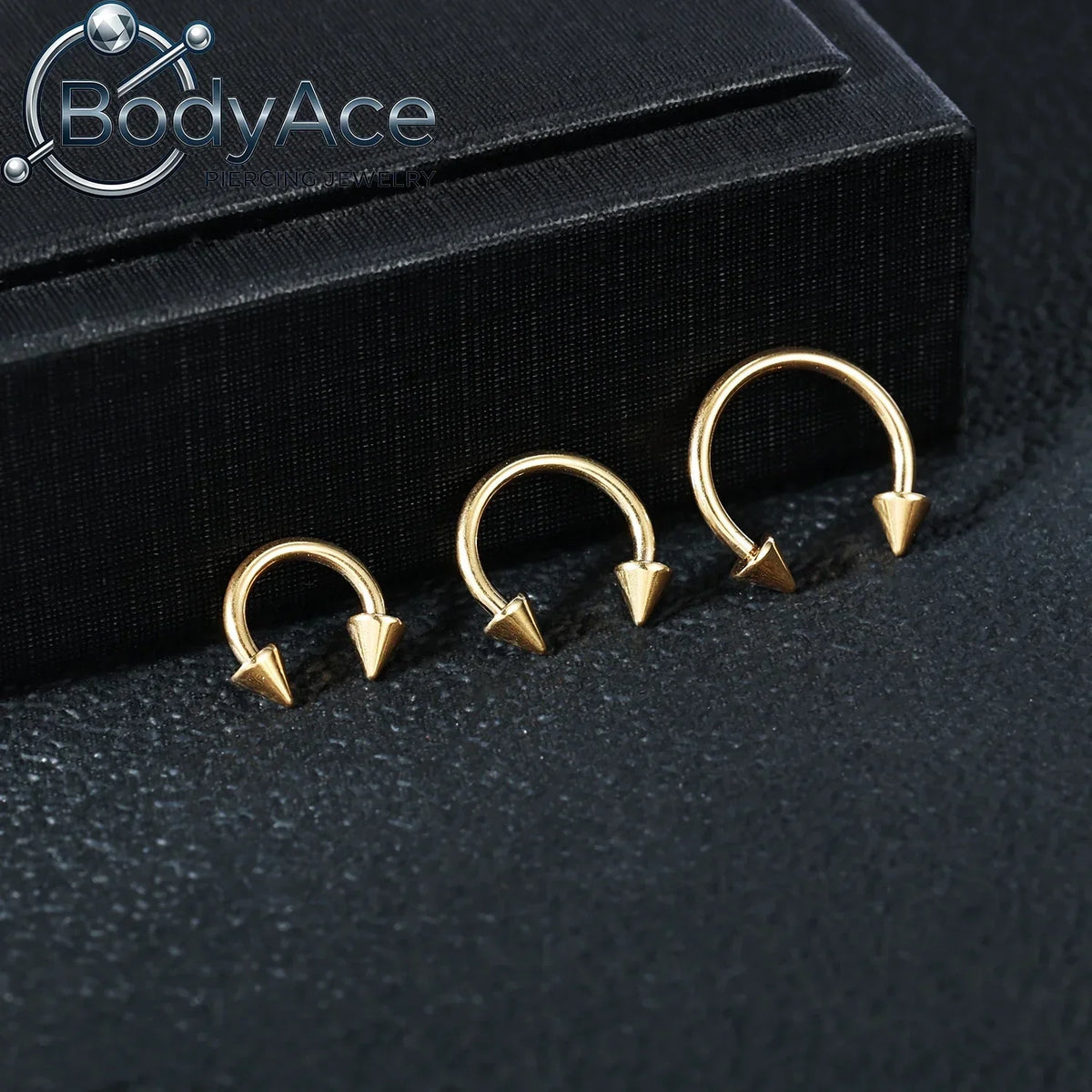 A set of gold-colored titanium steel nose rings with CZ crystals displayed on a black surface.