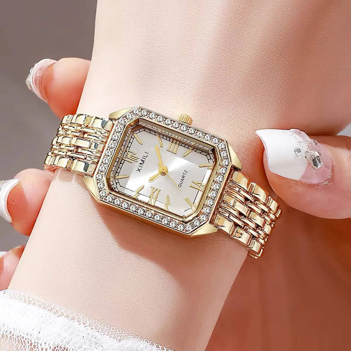A gold-toned rhinestone quartz wristwatch with a square face and metal bracelet worn on a person's wrist.