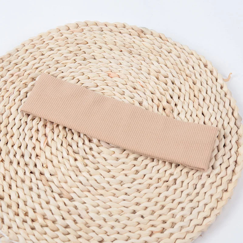 A beige knitted elastic headband lying on a woven natural fiber mat.