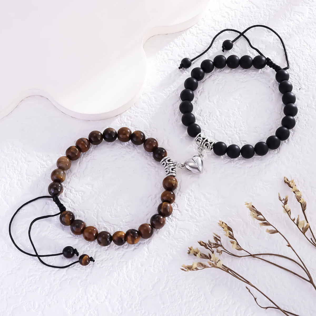 Two beaded bracelets made of natural brown and black stones with silver heart charms displayed on a white surface.