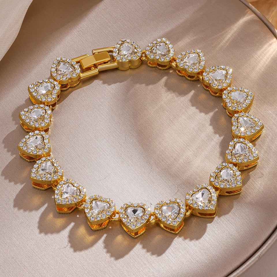 A gold-toned stacking bracelet set featuring multiple heart-shaped clear rhinestones on a neutral background.