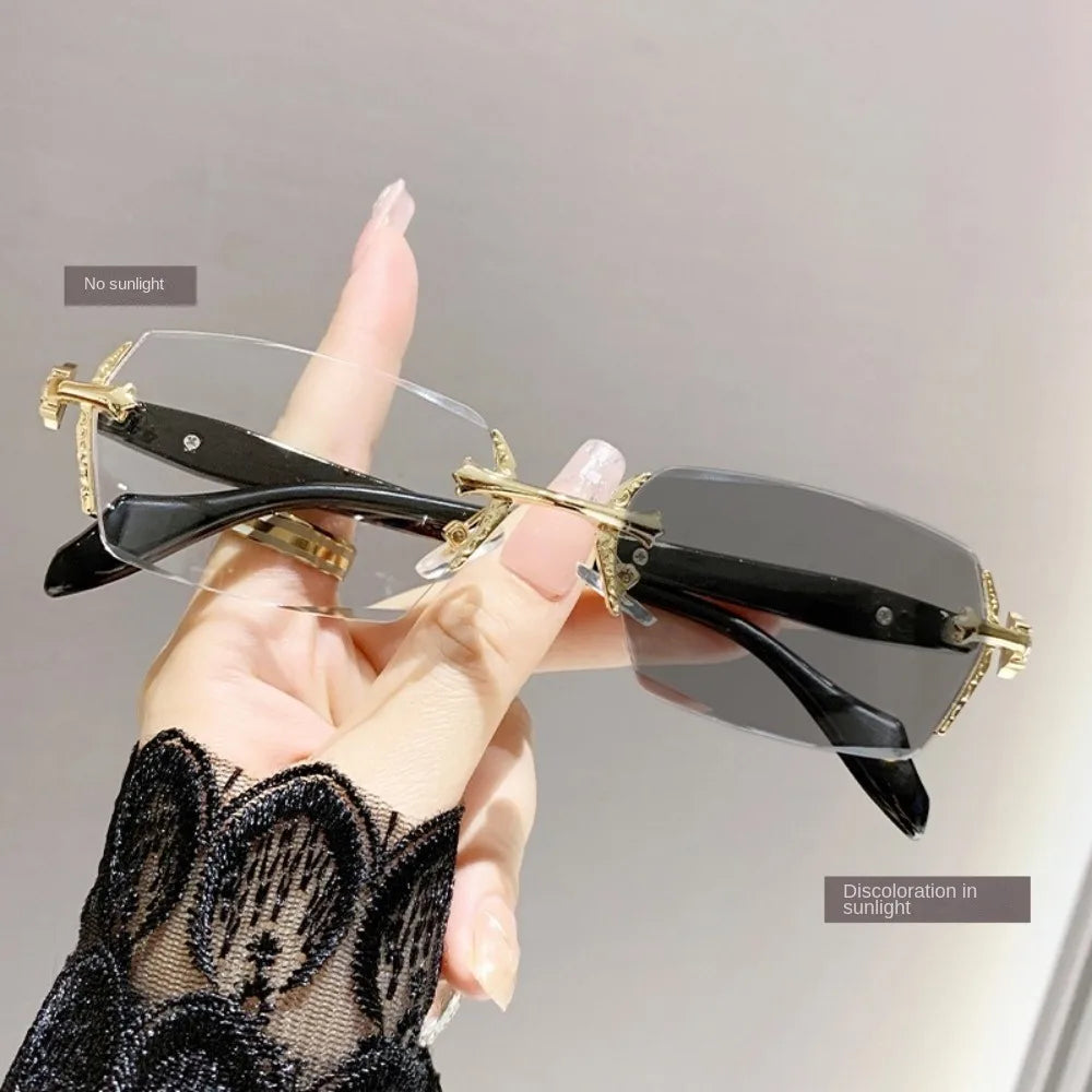 A hand holds a pair of black vintage Y2K frameless glasses with gold accents, demonstrating no discoloration in sunlight.