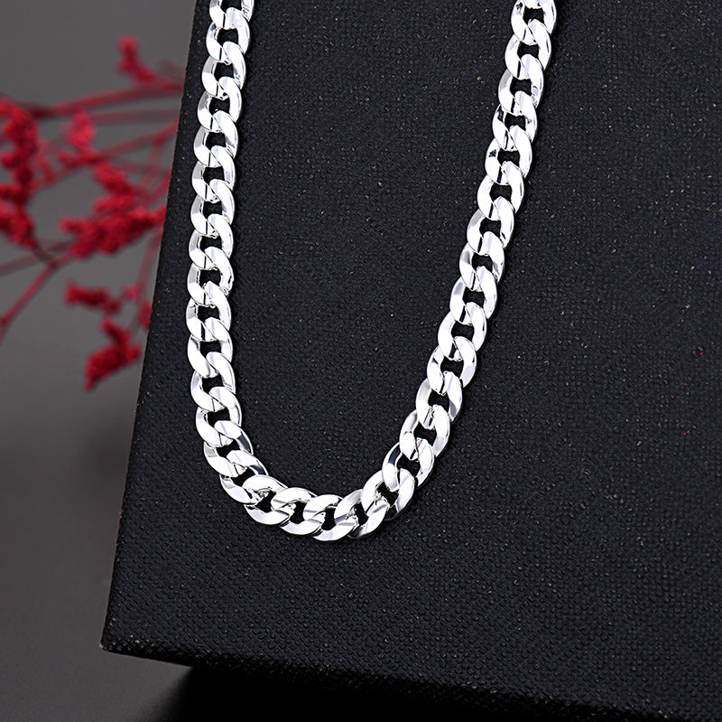 Un collier de chaîne argentée est exposé sur une surface noire à côté d'une branche florale rouge.