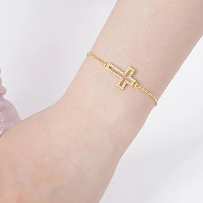A close-up of a gold plated cross bracelet with cubic zirconia on a wrist.