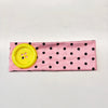 Pink fabric headband with black polka dots and a yellow button detail