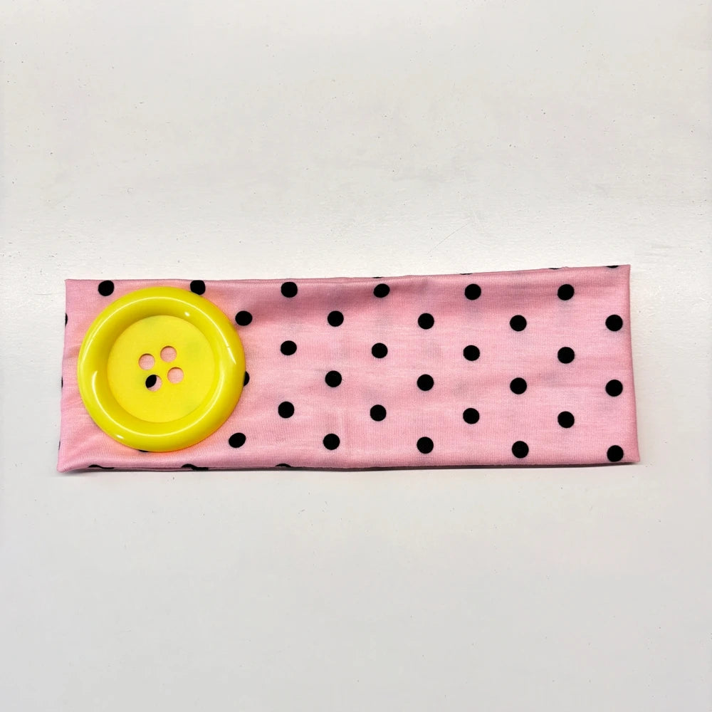 Pink fabric headband with black polka dots and a yellow button detail