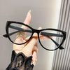 Eine Hand hält eine schwarze Vintage Cat-Eye-Lesebrille mit goldenen Akzenten vor einem hellen Hintergrund.