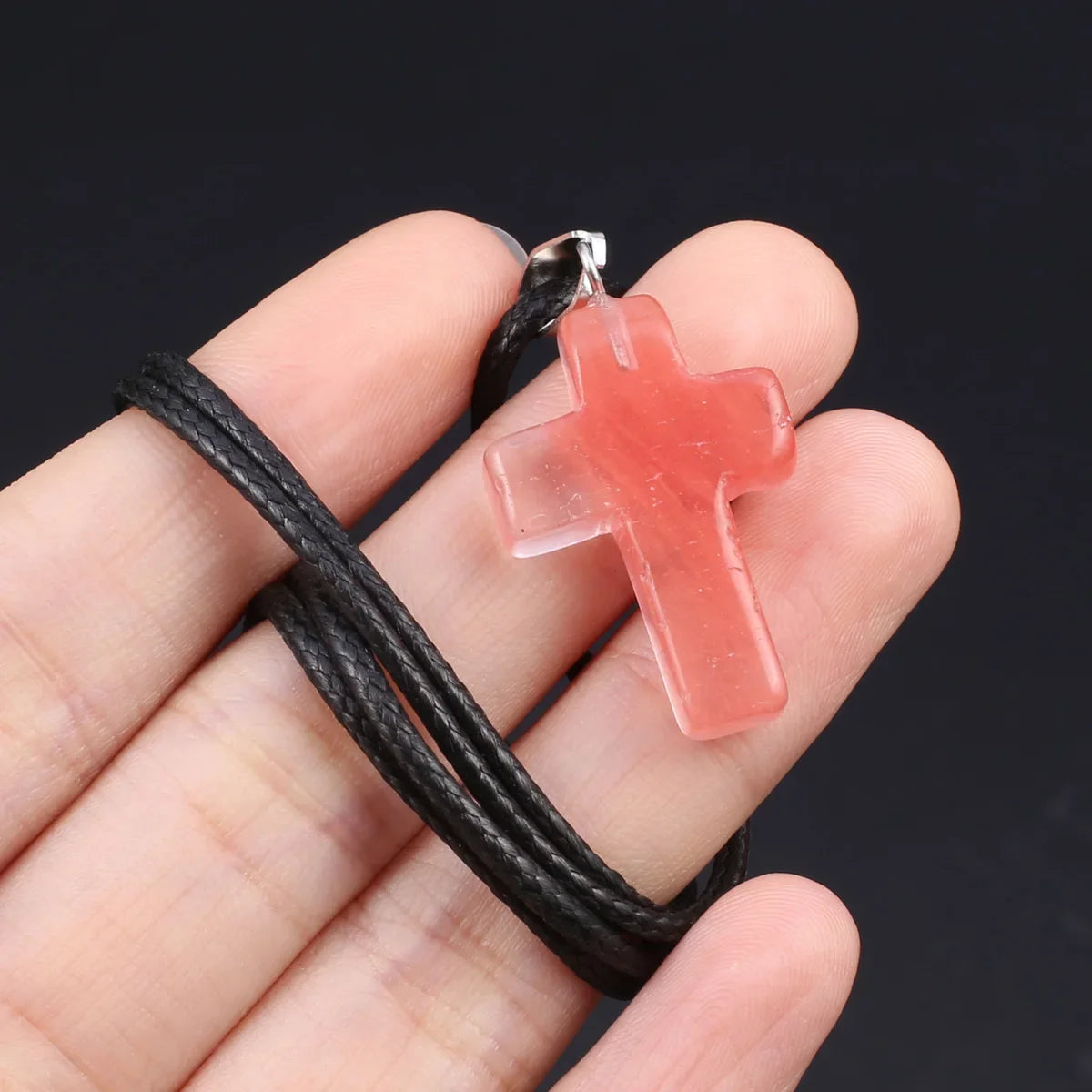 Eine Hand hält eine rosa Tigerauge-Agat-Kreuz-Anhängerkette auf einem schwarzen Band.