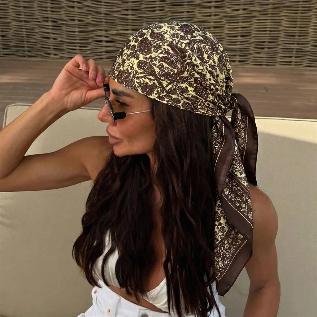 A woman wearing a leopard print silk scarf and sunglasses, looking over her shoulder.