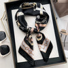 Black silk scarf and headband set featuring gold-toned hardware and patterned fabric displayed in a dark frame.