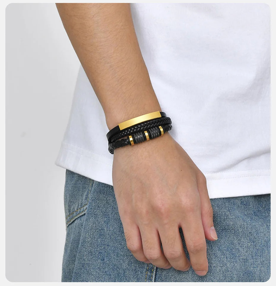 Nahaufnahme von einem Handgelenk mit schwarzem und goldenem geflochtenem Lederarmband vor weißem Hemd und blauen Jeans.