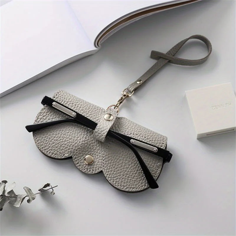 A light gray PU leather pouch and glasses case with a leather strap resting on a white surface.