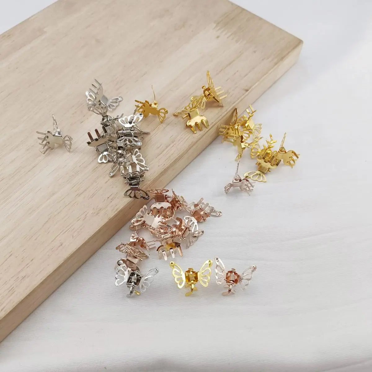 A set of ten mini hollow butterfly metal hair clips in various gold and silver finishes displayed on a wooden board.