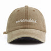 A beige washed baseball cap with white embroidered text that reads overstimulated
