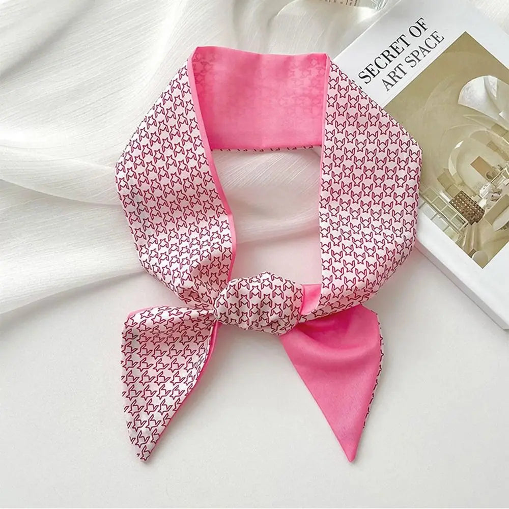 Diadema de seda rosa con flor, pañuelo atado en lazo, sobre una superficie blanca junto a un libro.