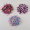 Three piles of colorful disposable rubber hair ties in various shades of pink, purple, and blue.