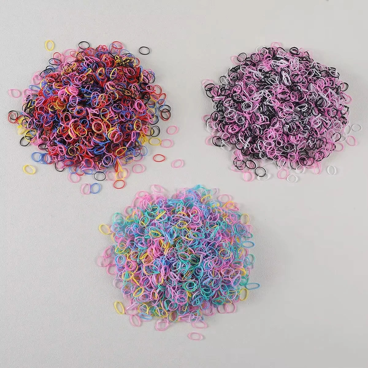 Three piles of colorful disposable rubber hair ties in various shades of pink, purple, and blue.