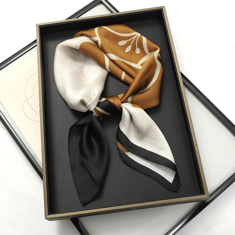 A folded luxury silk scarf in shades of beige, brown, and black displayed in a square wooden frame.