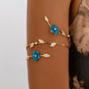 A gold-toned floral vine arm bracelet featuring blue enamel flowers and gold leaf accents on a person's wrist.