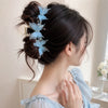 A woman's dark hair is styled in an updo with a pearl rhinestone butterfly hair claw clip featuring light blue flowers.