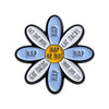 A flower brooch set with ten enamel petals, each engraved with a different phrase like Get Shit Done or Eat Tacos.