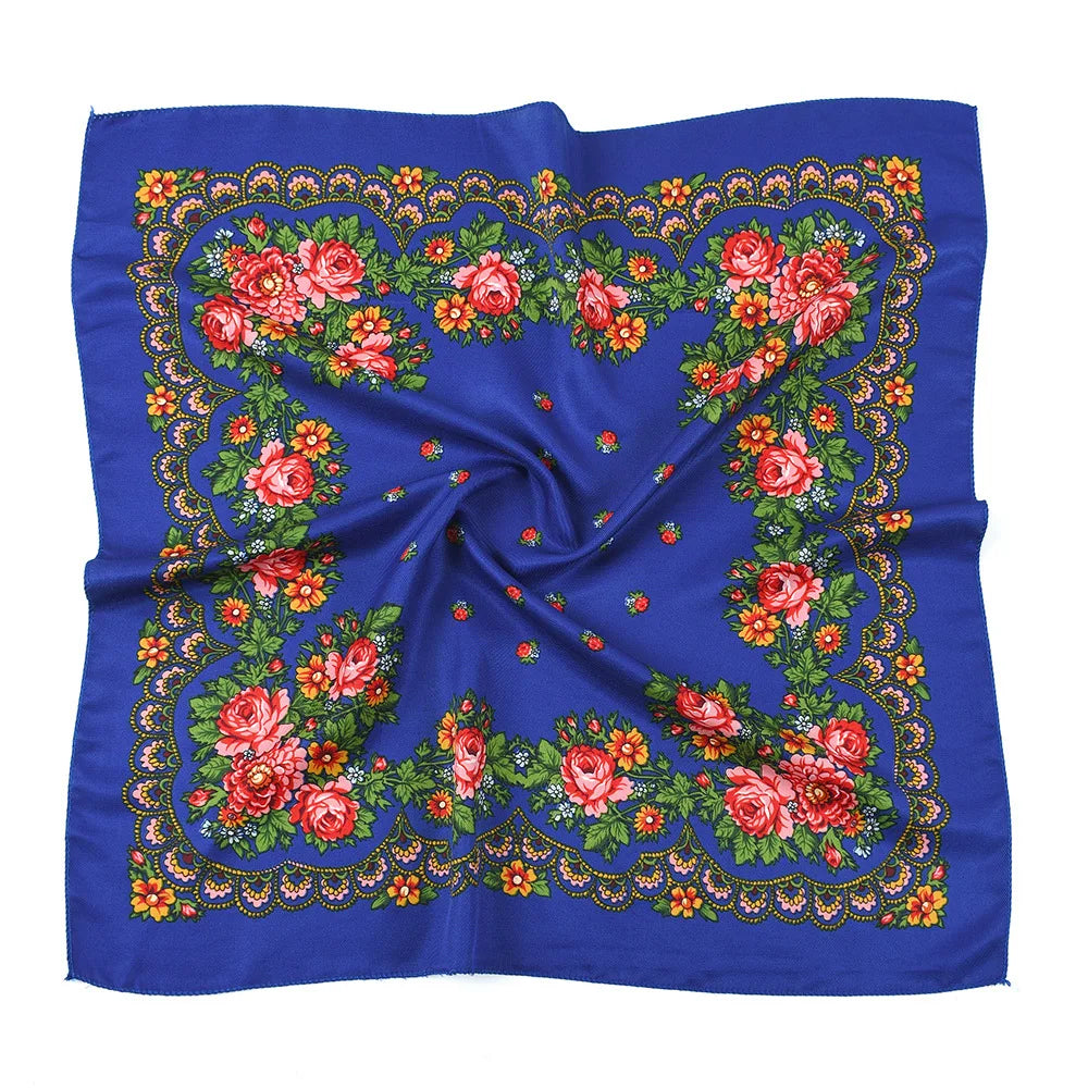 A vibrant blue silk scarf featuring an intricate floral print with red, pink, and orange roses and green leaves.